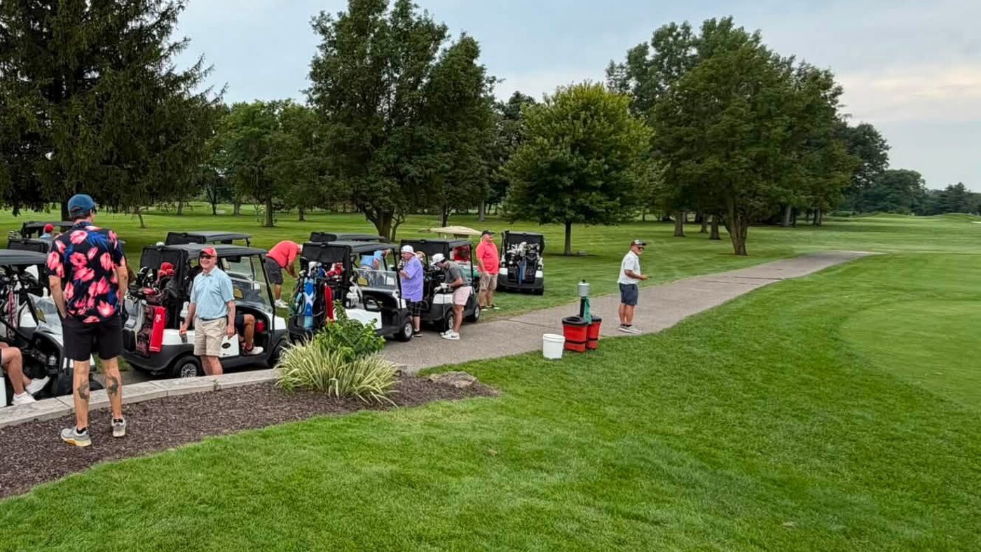 Golf carts lined up along the path before a round, players gathering on the course